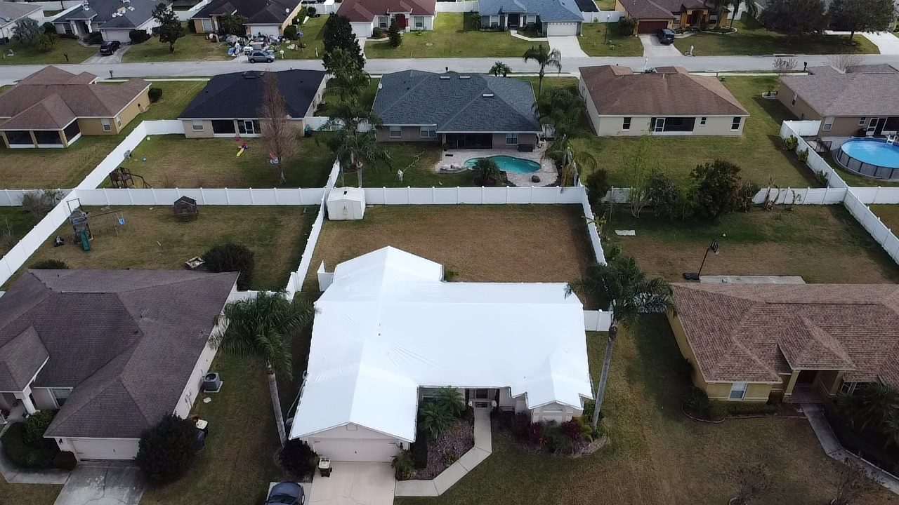Aerial view of a single-storey home with its whole roof sealed in white shrink wrap, fenced yards and pools around it
