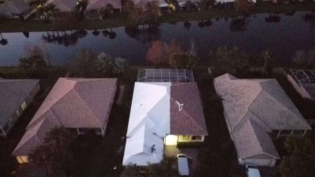 White shrink wrap covering a roof between two tile-roofed neighbors, canal water behind the properties