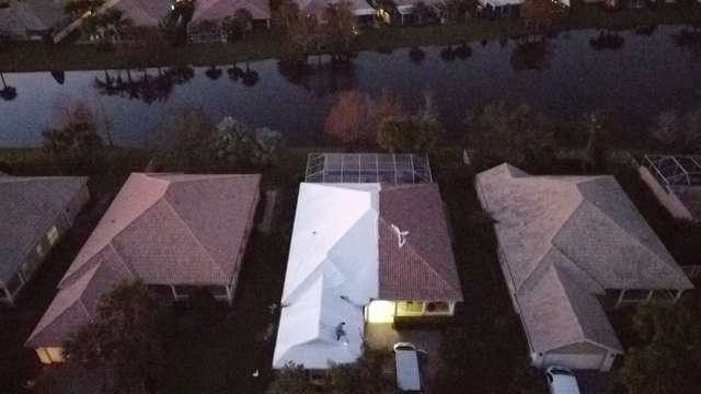White shrink wrap covering a roof between two tile-roofed neighbors, canal water behind the properties