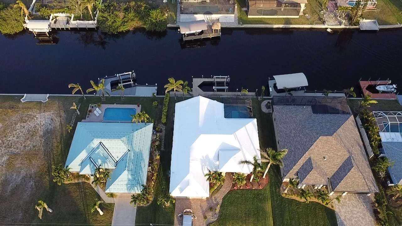 Waterfront home with its roof wrapped in white, pool cage and canal dock below