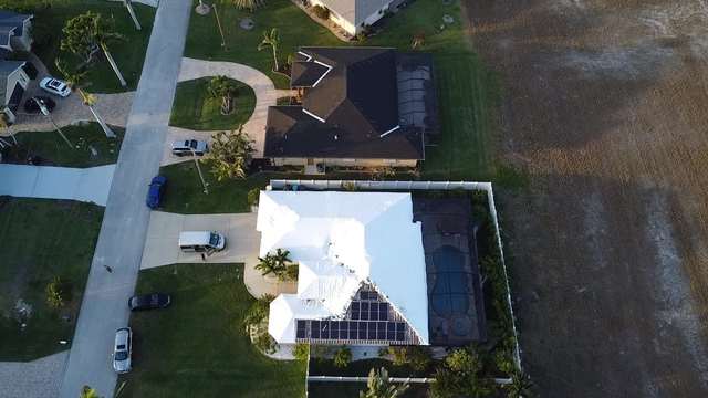 Corner-lot home from above with the full roof shrink wrapped, street and driveway alongside
