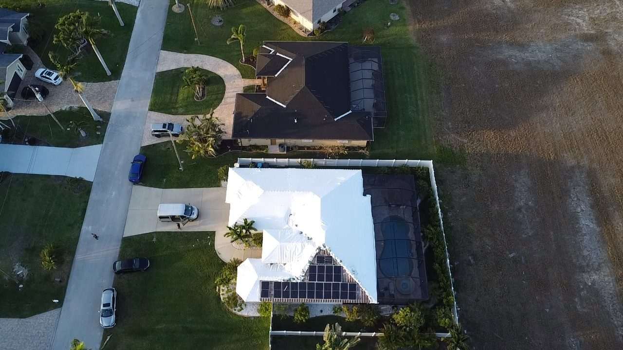 Corner-lot home from above with the full roof shrink wrapped, street and driveway alongside