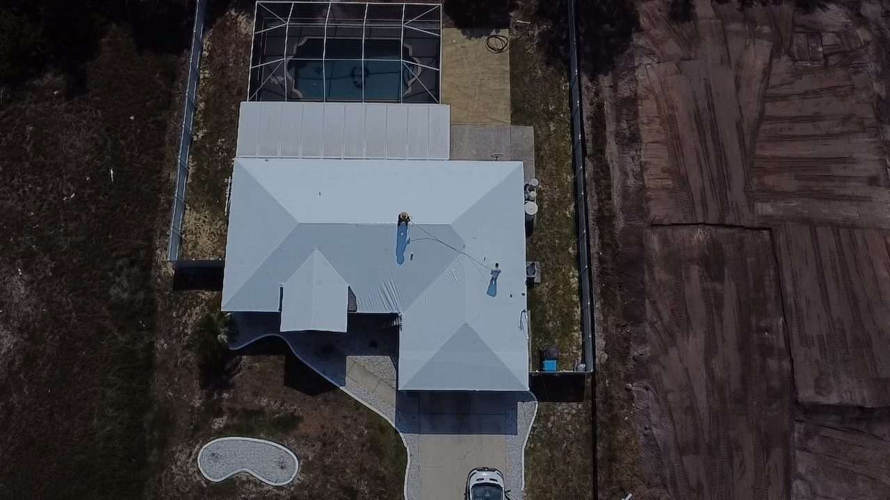 White-wrapped roof next to a screened pool, turned earth on the lot alongside