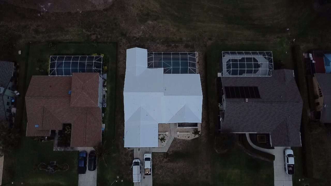 Two-storey home wrapped in white between a tile roof and a shingle roof, cars in both driveways
