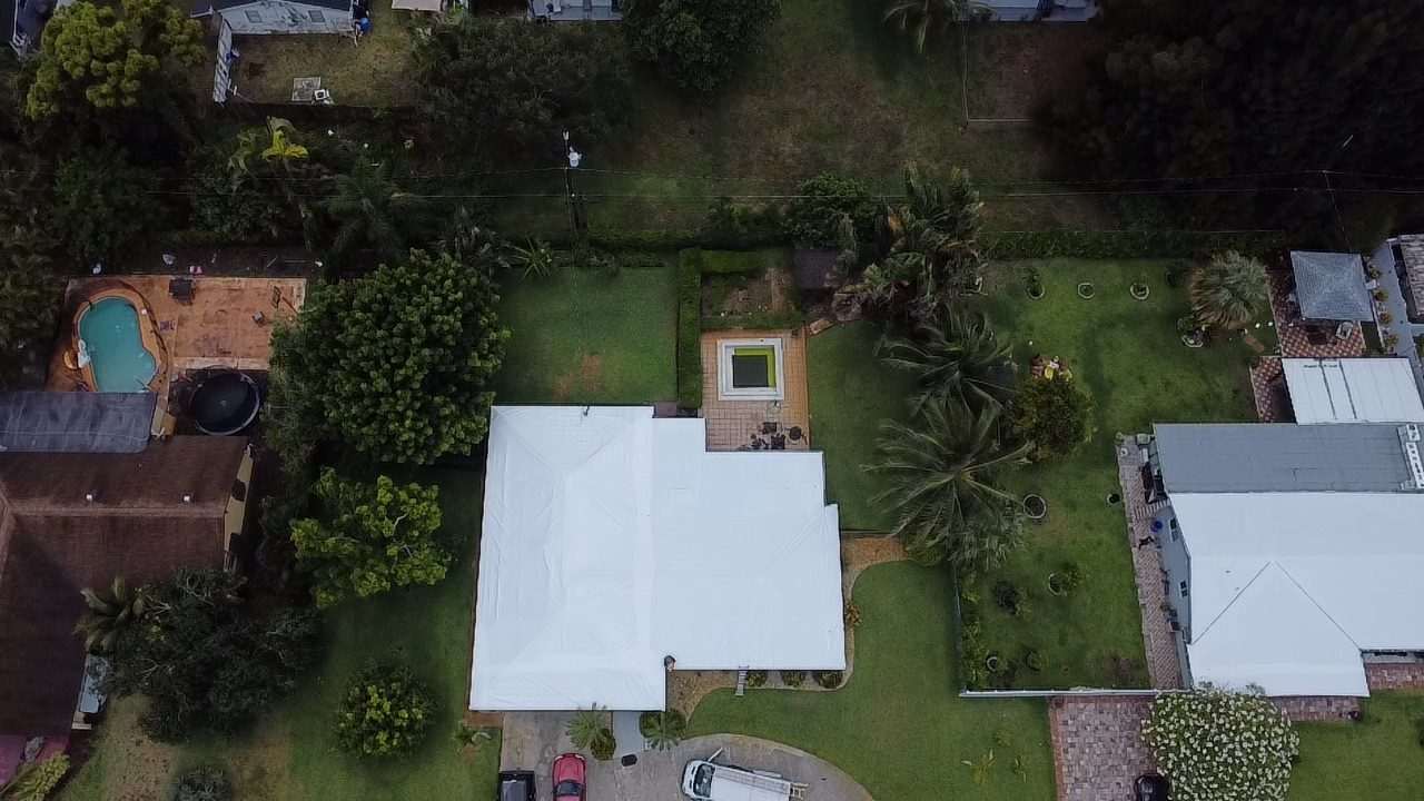 Wrapped roof on a wooded lot, pool and garden visible through the palms