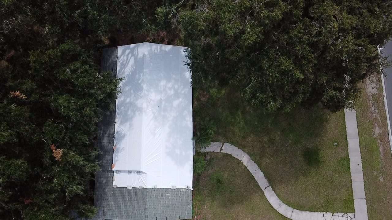 Long narrow roof sealed in white shrink wrap, framed by trees on both sides