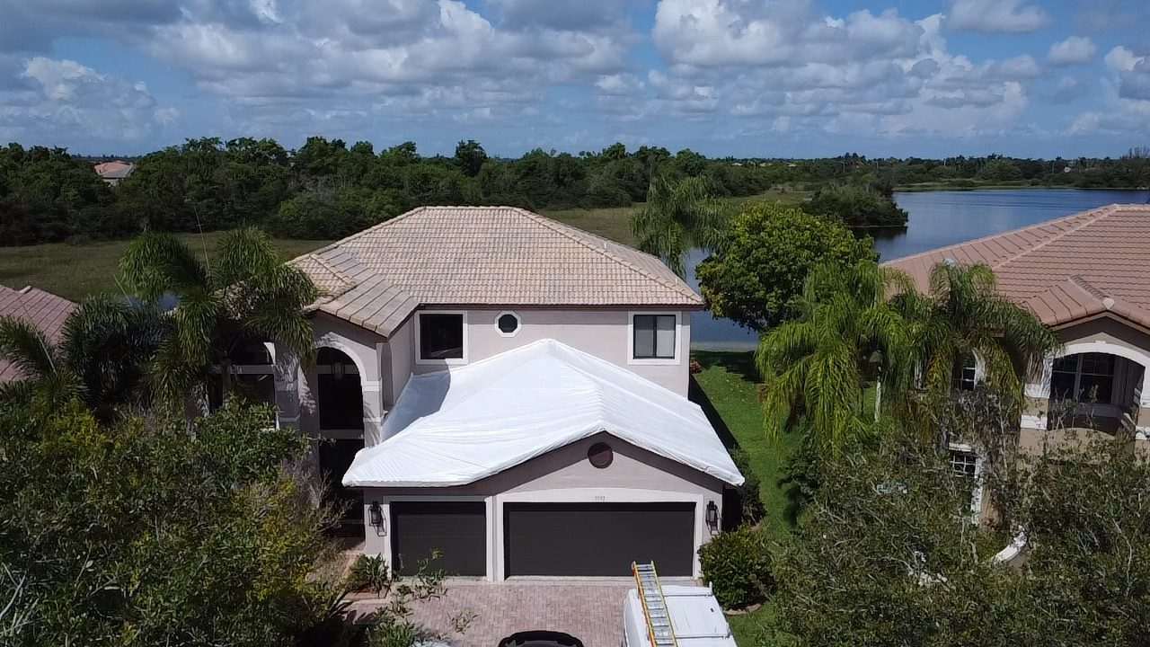 Two-storey lakefront home with the front roof section wrapped in white, ladder set against the gable