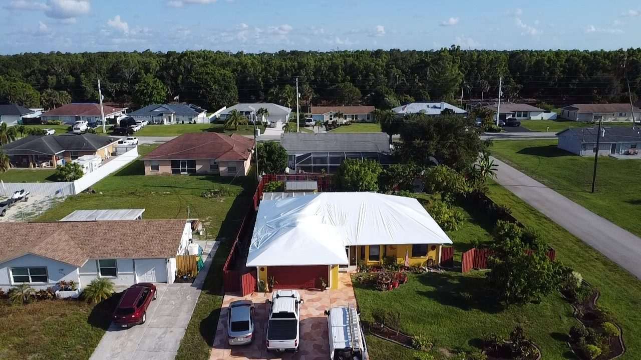 Yellow single-storey home with its roof fully wrapped, cars and a work van in the driveway