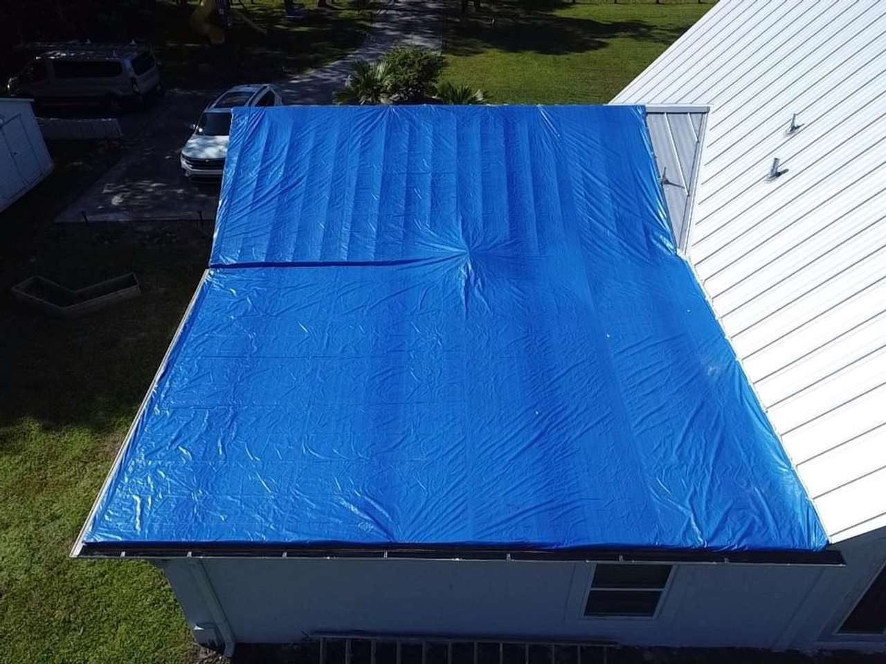 Blue emergency tarp pulled tight over one slope of a low-pitched roof and weighted along the seam