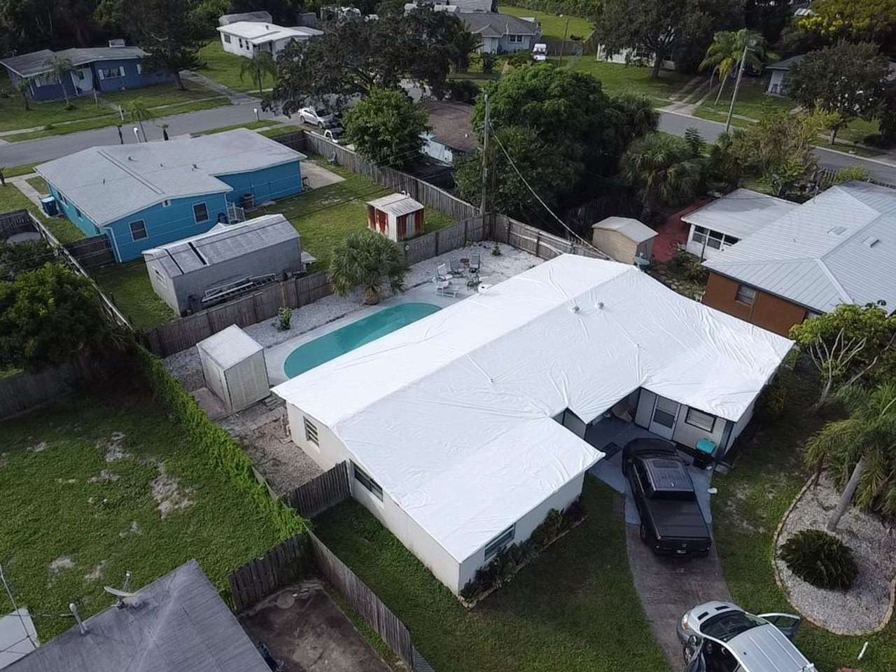 Two adjoining roof sections sealed in white wrap, pool and screened patio behind