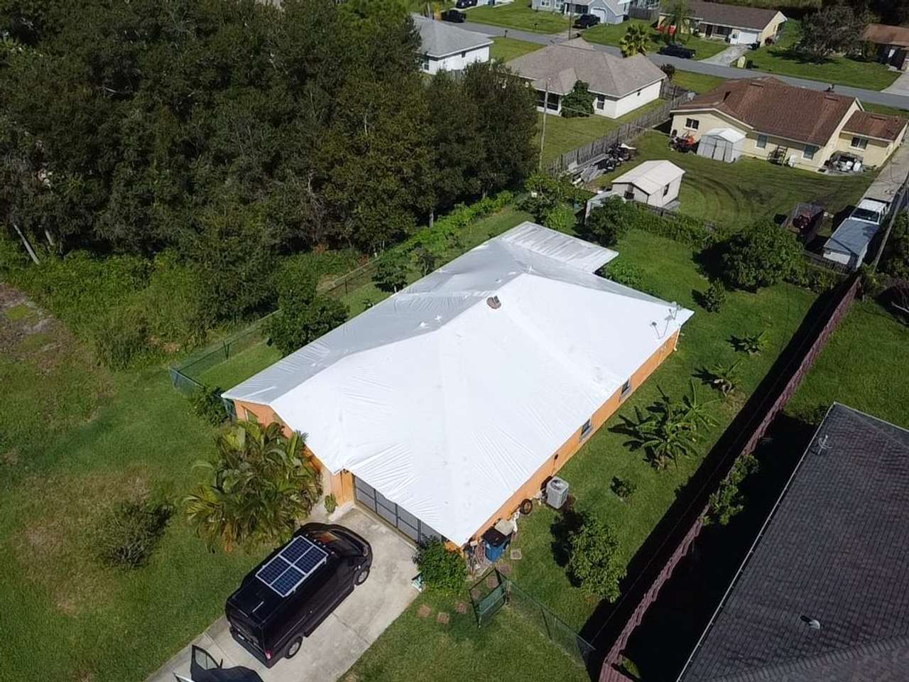 White-wrapped roof over an orange-walled home, driveway and van below