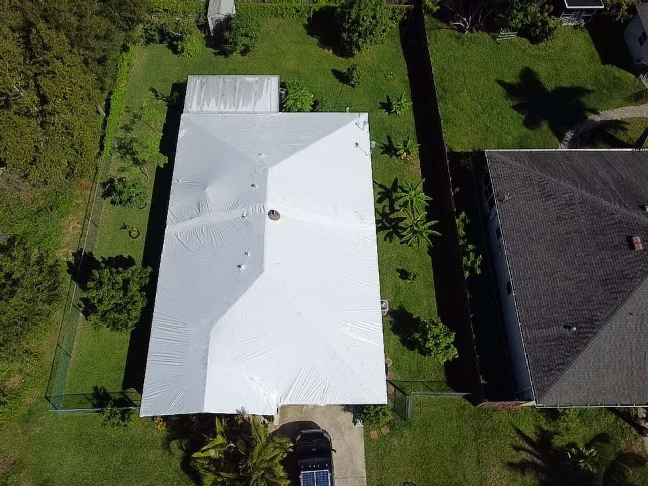 Large hipped roof completely covered in white shrink wrap, seen from above