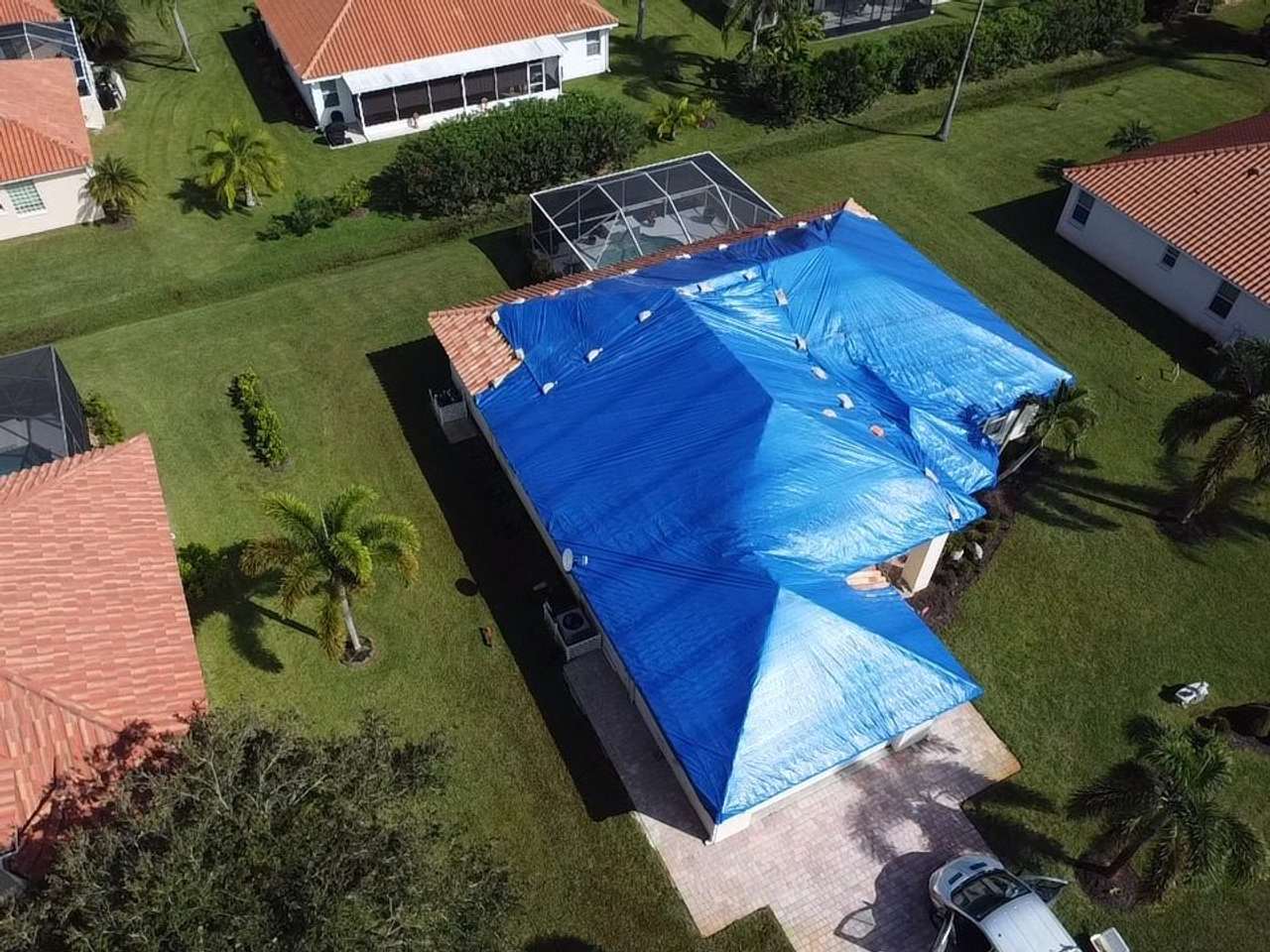 Blue emergency tarp covering a barrel tile roof next to a screened pool cage