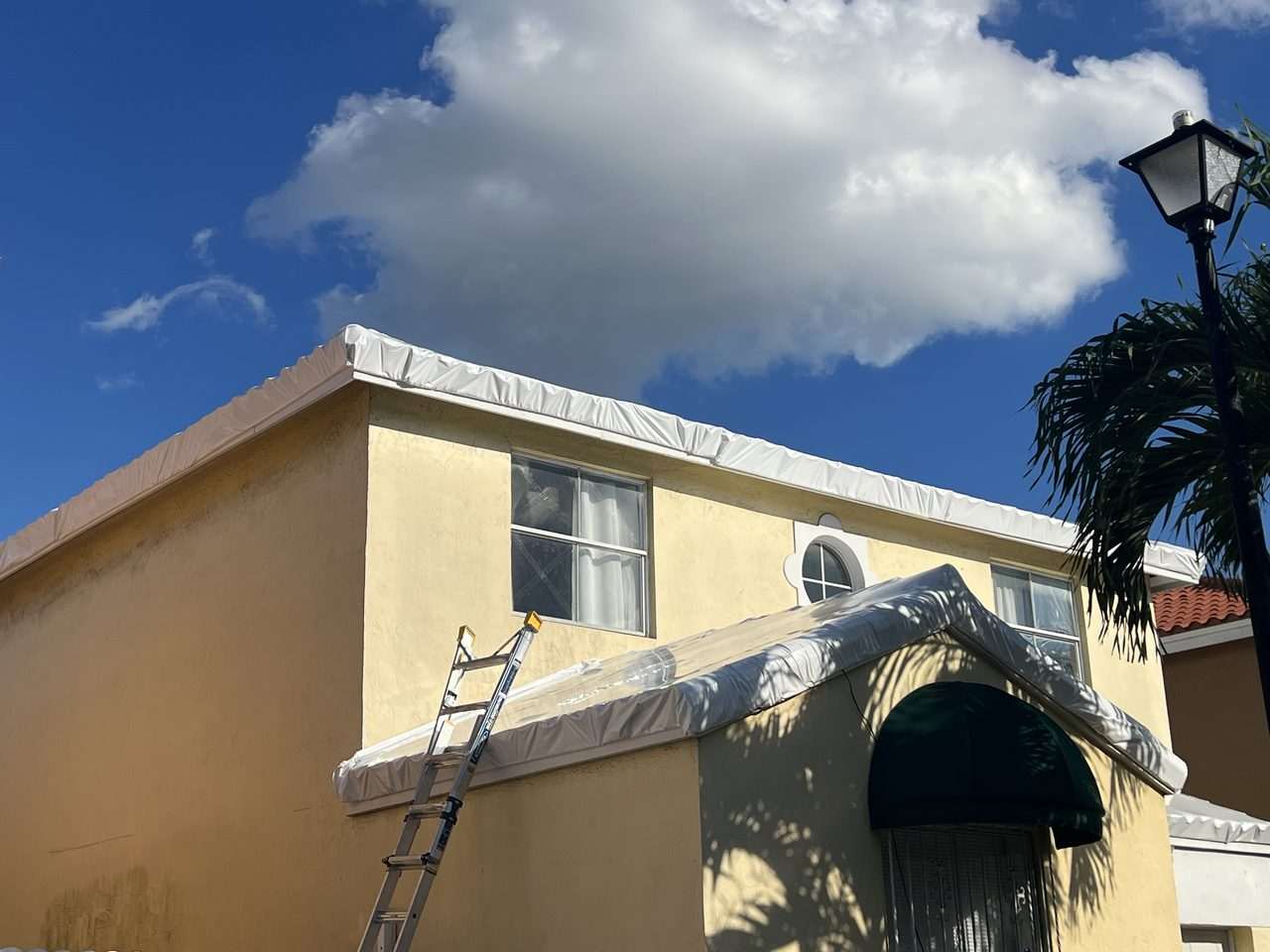 Shrink wrap fitted along the gable end of a two-storey home, ladder standing against the wall