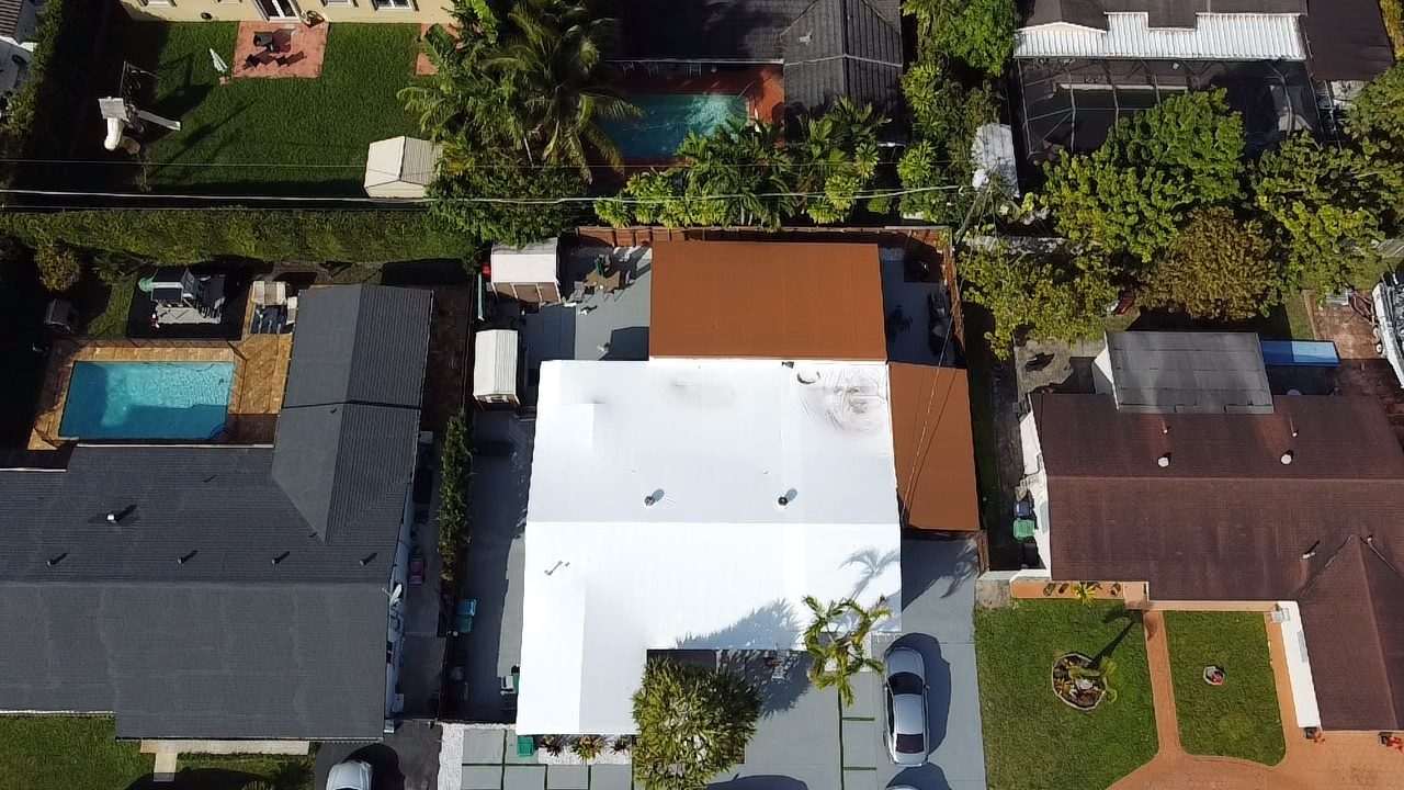 White-wrapped roof between a grey shingle roof and an orange tile one, pool in the next yard